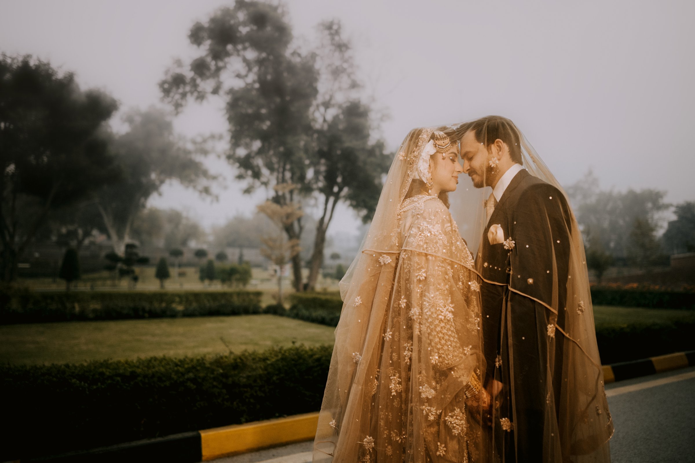 Couple beneath one veil in a misty garden